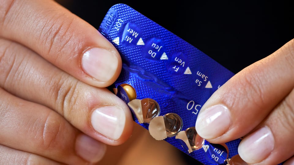 Frauenhände nehmen eine Pille aus einem blauen Blister.