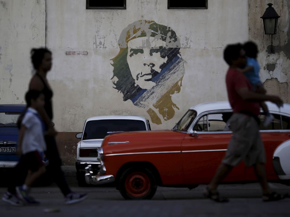 Zu sehen ist ein Graffiti des kubanischen Revolutions-Helden Che Guevarra - davor laufen kubanische Bürger der Strasse entlang
