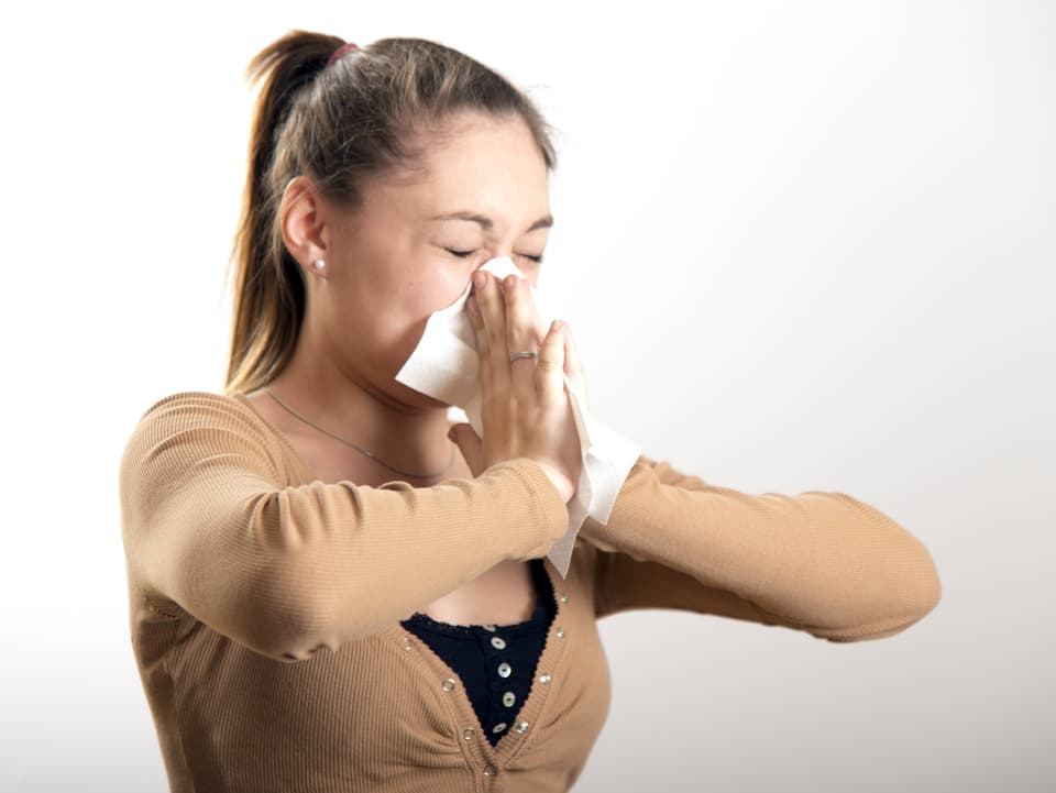 Junge Frau niest in ein Taschentuch