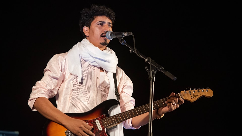 A young musician sings and plays bass on stage.