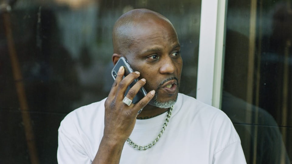Eine Person of Color steht vor einem Fenster und telefoniert mit dem Handy
