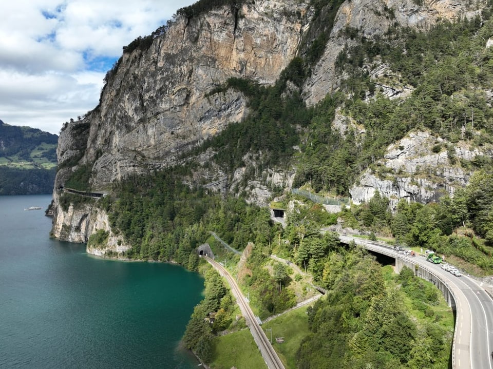 Estrada costeira e túnel ferroviário ao longo de um lago e rochas.