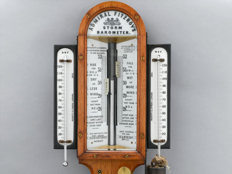 Ein originales Barometer aus den Zeiten von Fitzroy. Ein hölzerner Rahmen mit den Instrumenten auf weissem Hintergrund.