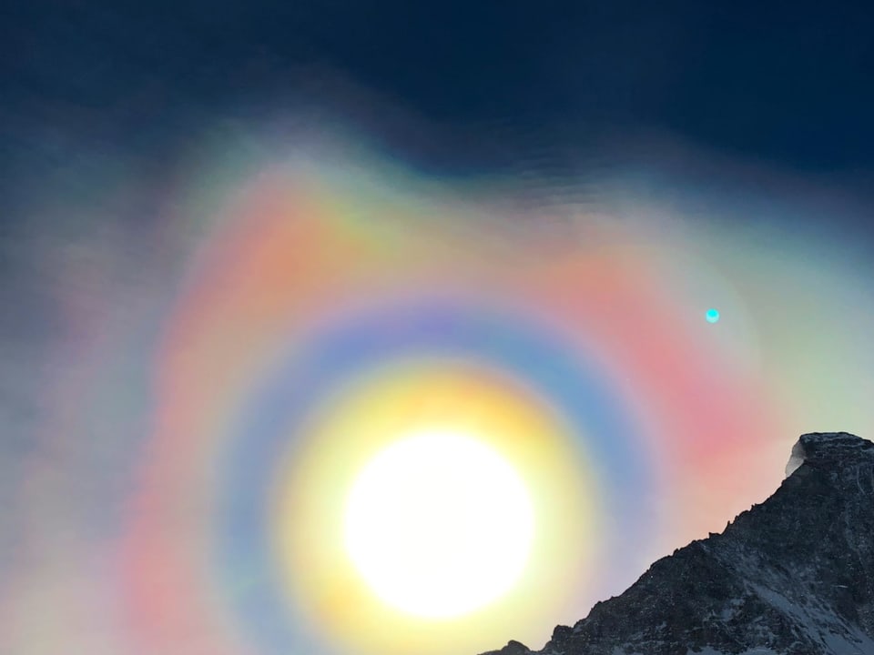 Rund um die Sonne, sie steht neben dem Matterhorn am Himmel, hat sich scheibenförmig eine sogenannte Korona gebildet. Sie schillert in gelb,gold, blau, grün und rosarot.
