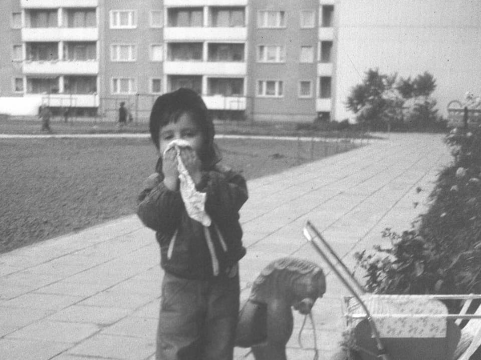 Kleines Mädchen mit Puppenwagen vor einem DDR-Neubaublock. (Schwarz-Weiss-Bild)
