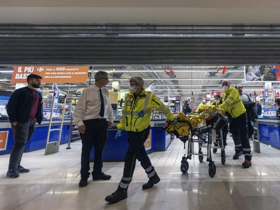 Rettungspersonal mit Leuchtuniform schieben und ziehen eine Bahre mit einer verletzten Person.