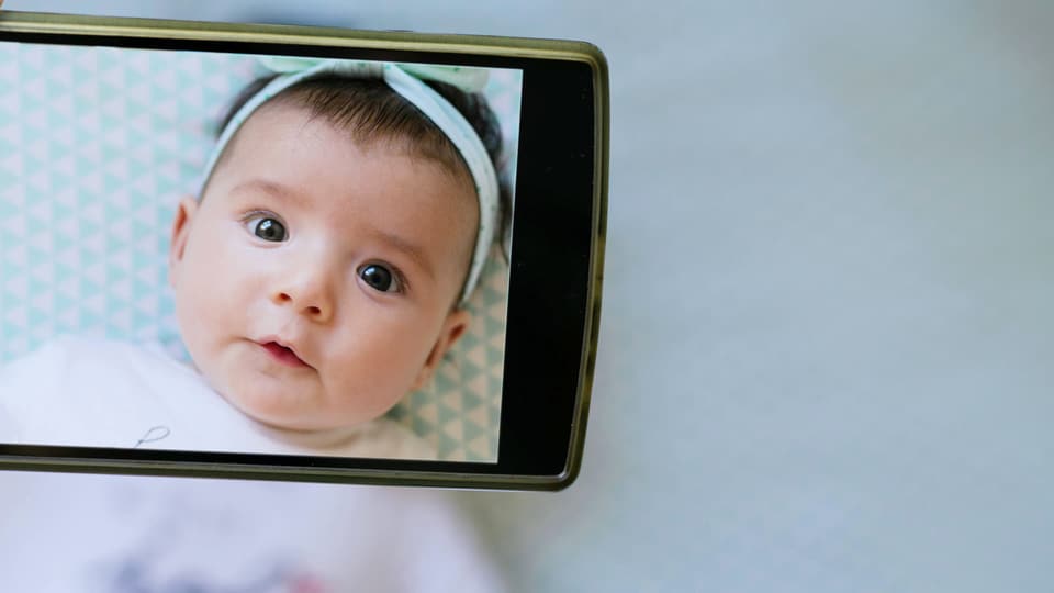 Ein Baby durch die Kamera eines Smartphone betrachtet.