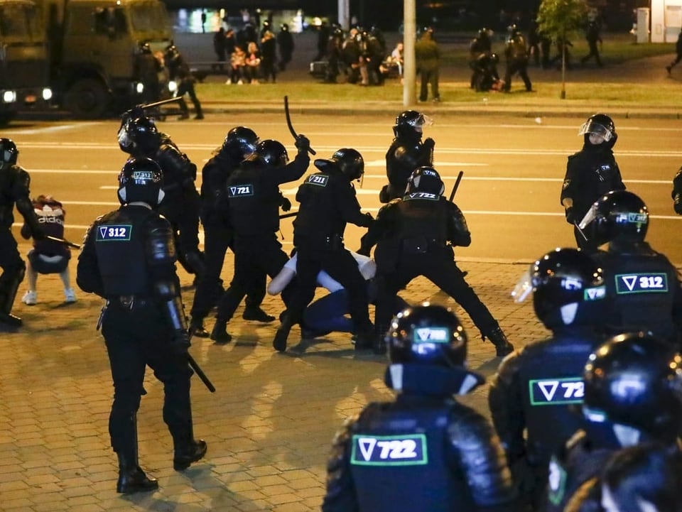 Uniformierte Polizisten prügeln mit Schlagstöcken auf Protestierende ein.