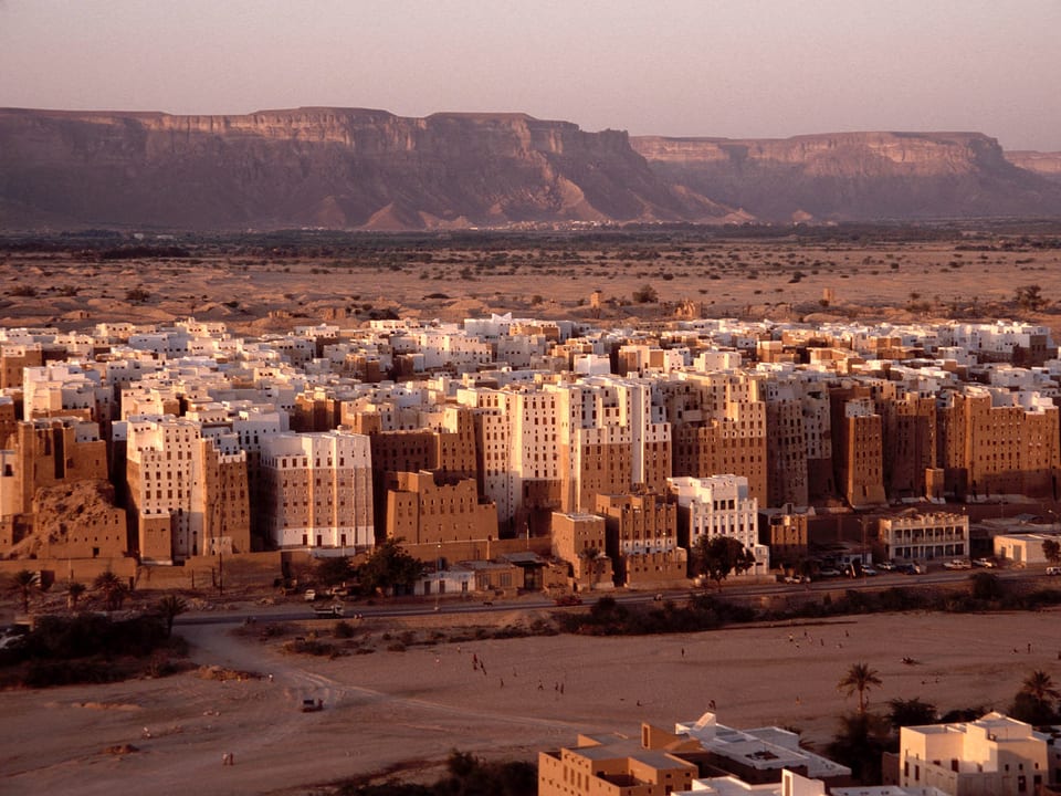 Blick auf eine Stadt in der Wüste. Die Gebäude sind mehrstöckig und aus Lehm. 