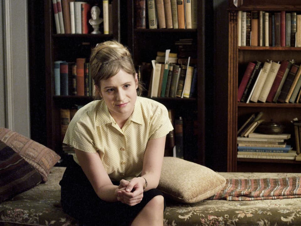 Die Schauspielerin Julia Jentsch sitzt auf einem Bett vor einem grossen Bücherregal und blickt freundlich aus dem Bild.