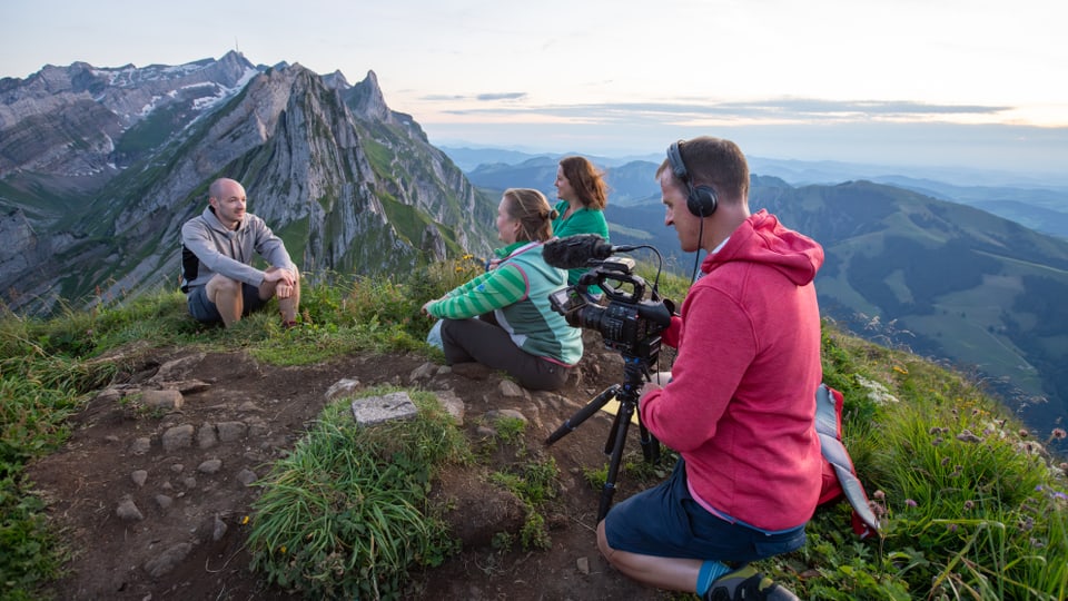 Der Naturjodler Meinrad Koch sitzt auf einem Berggipfel, wo er für die Doku von den zwei Regisseurinnen interviewt wird.