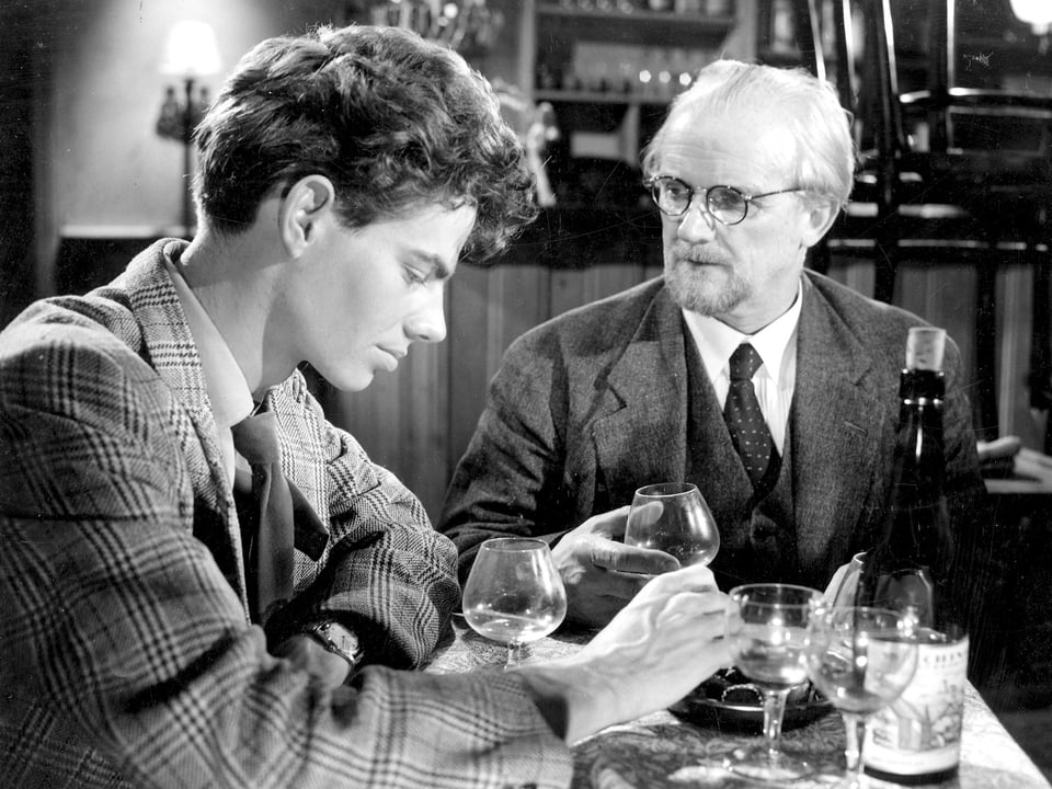 Ein junger Mann sitzt mit einem älteren Mann am Tisch. Sie trinken Wein.