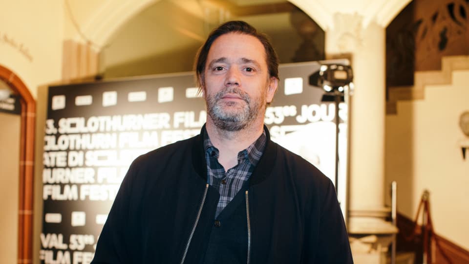 Ein Mann mit grauem Bart vor einer Werbetafel der Solothurner Filmtage.