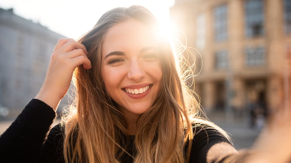 Eine hübsche junge Frau lächelt in die Kamera, die Sonne umspielt ihr Gesicht.